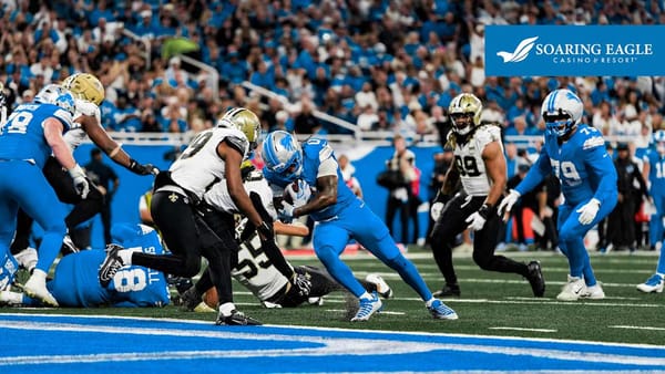 Jahmyr Gibbs carrying the ball through Saints defenders during a Detroit Lions game.